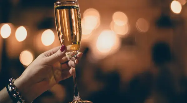Mano con smalto rosso tiene un calice di champagne extra dry, con luci sfocate sullo sfondo.
