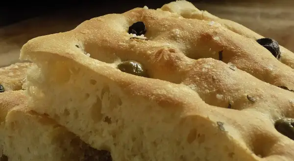 Focaccia soffice con olive e rosmarino, perfetta da gustare con un buon vino.