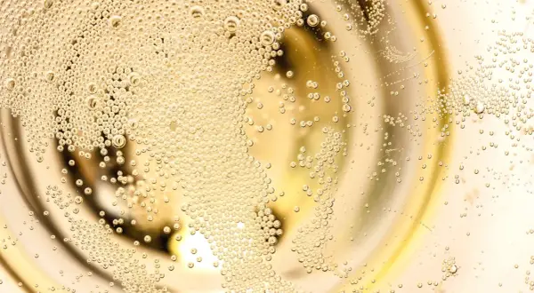 Bollicine dorate salgono in un bicchiere, evocando la freschezza di un Franciacorta Prosecco.