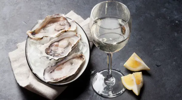 Piatto di ostriche fresche su ghiaccio, accompagnato da un bicchiere di vino francese per ostriche e spicchi di limone.