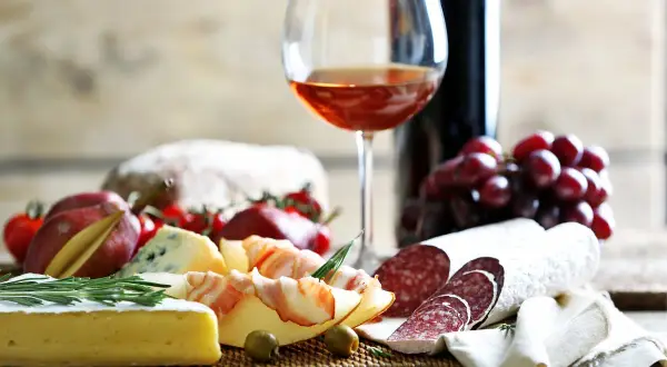 Tagliere con salumi, formaggi, uva e pane. Un bicchiere di vino rosato suggerisce perfetti vermentino abbinamenti.