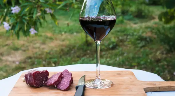 Un bicchiere di vino rosso e salumi affettati su un tagliere di legno, perfetti per le associazioni vini e salumi naturali.