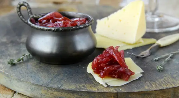 Un delizioso abbinamento formaggi marmellate e vino: formaggio stagionato con cipolle rosse caramellate, pronto per essere gustato.
