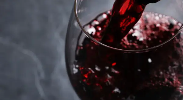 Versando vino rosso rubino in un calice, evocando i sapori autentici dei vini lucani.