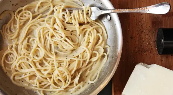 Spaghetti cacio e pepe cremosi, pronti per un perfetto abbinamento vino. Pepe macinato fresco e pecorino a lato.