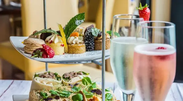 Delizioso abbinamento champagne con pasticcini, macarons, fragole e tartine su un elegante espositore a più livelli.