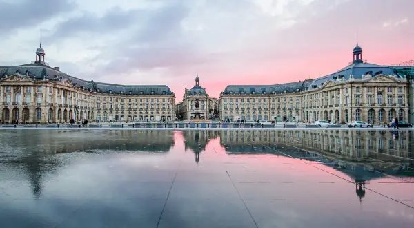 Piazza specchiata al tramonto, con edifici eleganti che ricordano il fascino del Medoc Bordeaux.
