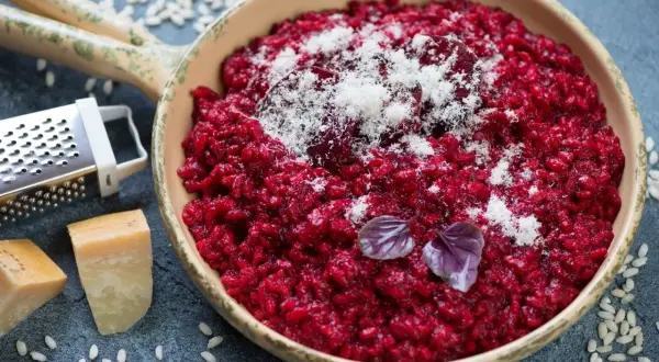 Risotto rosso vibrante, guarnito con parmigiano grattugiato e basilico. Accanto, ingredienti per un perfetto vino rosso per risotto.