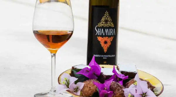 Calice di passito di Pantelleria accanto a dolcetti e fiori viola.