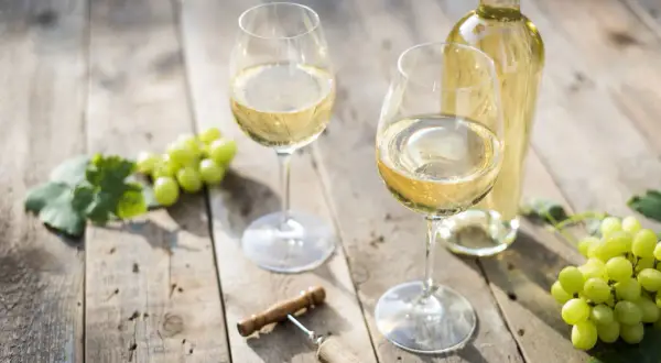 Due calici di vino bianco, una bottiglia, uva e cavatappi su un tavolo di legno. Le caratteristiche del Pouilly-Fumé si riflettono in questo scenario.