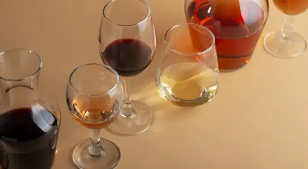 Bicchieri e caraffe con vino rosso, bianco e rosato. Un bicchiere di vino rosso, forse un Merlot, risalta tra gli altri.