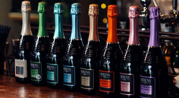 Una fila di bottiglie di Prosecco Serena, ognuna con un tappo colorato. Il brut è un Prosecco, perfetto per ogni occasione.