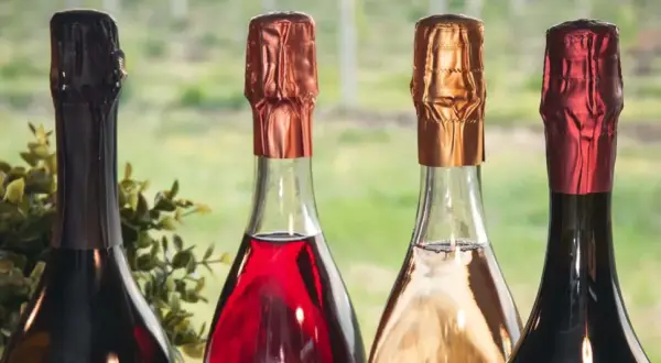 Quattro bottiglie di vini più pregiati, con tappi color rame, oro e rosso, pronte per essere degustate.