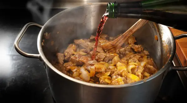 Carne e cipolle in cottura in una pentola, con vino rosso versato da una bottiglia. Un classico per le ricette con il vino rosso.