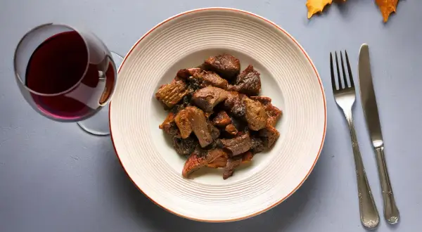 Piatto di cinghiale in umido con un bicchiere di vino rosso, perfetto vino da abbinare al cinghiale.