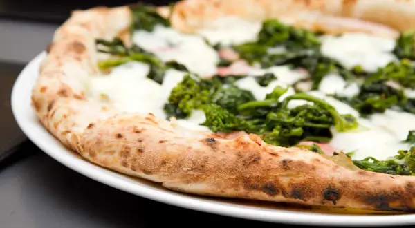 Pizza con verdure e mozzarella su un piatto bianco, un'ottima scelta per una serata con pizza e champagne.
