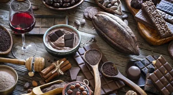 Un bicchiere di vino rosso accompagna una ricca selezione di cioccolato, dai chicchi di cacao alle tavolette, per un'esperienza golosa.
