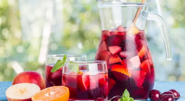 Caraffa e bicchieri pieni di sangria, con frutta fresca come mele, arance e ciliegie. Perfetta per fare la sangria in una giornata estiva.