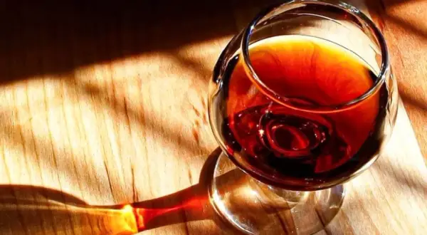 Un bicchiere di **marsala vino** ambrato riposa su un tavolo di legno, illuminato da raggi di sole che creano ombre suggestive.