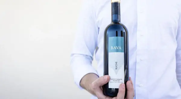 Uomo in camicia bianca tiene una bottiglia di vino Ruche di Castagnole Monferrato BAVA.
