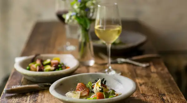 Deliziosi piatti con pesce e verdure, perfetti per i pinot grigio abbinamenti. Un bicchiere di vino bianco attende accanto a un bouquet di fiori.