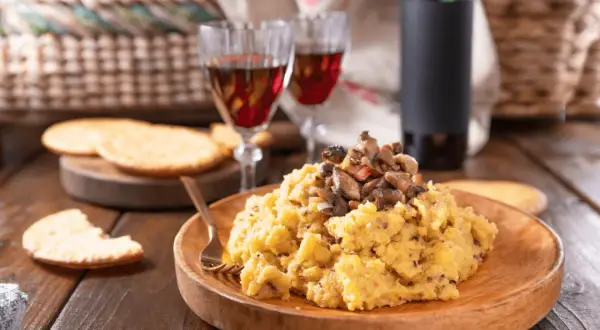 Polenta con funghi, perfetta con un buon vino da abbinare alla polenta. Due calici rossi e una bottiglia completano la scena rustica.
