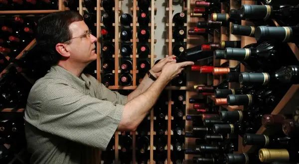 Uomo in cantina sceglie tra bottiglie di vino, tra cui uve cabernet.