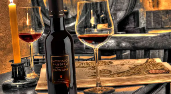 Una bottiglia e un calice di Moscato di Scanzo, illuminati da una candela, su un tavolo con una mappa antica.