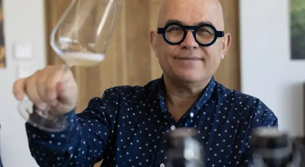 Uomo con occhiali rotondi tiene un bicchiere di champagne Francia, sorridendo.