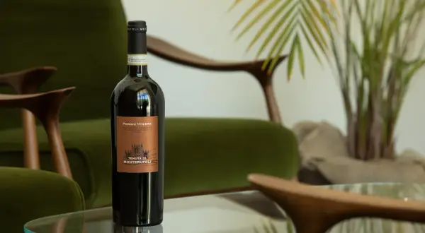 Bottiglia di vino umbro famoso, Poggio Miniera, su un tavolino di vetro, con poltrone verdi e una pianta sullo sfondo.