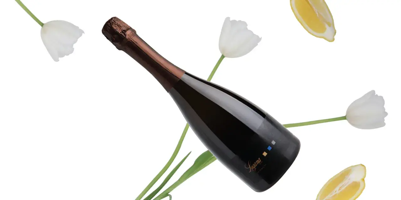 Bottiglia di spumante Trebbiano di Lugana tra tulipani bianchi e fette di limone, con un'etichetta che riporta il nome "Lugana".