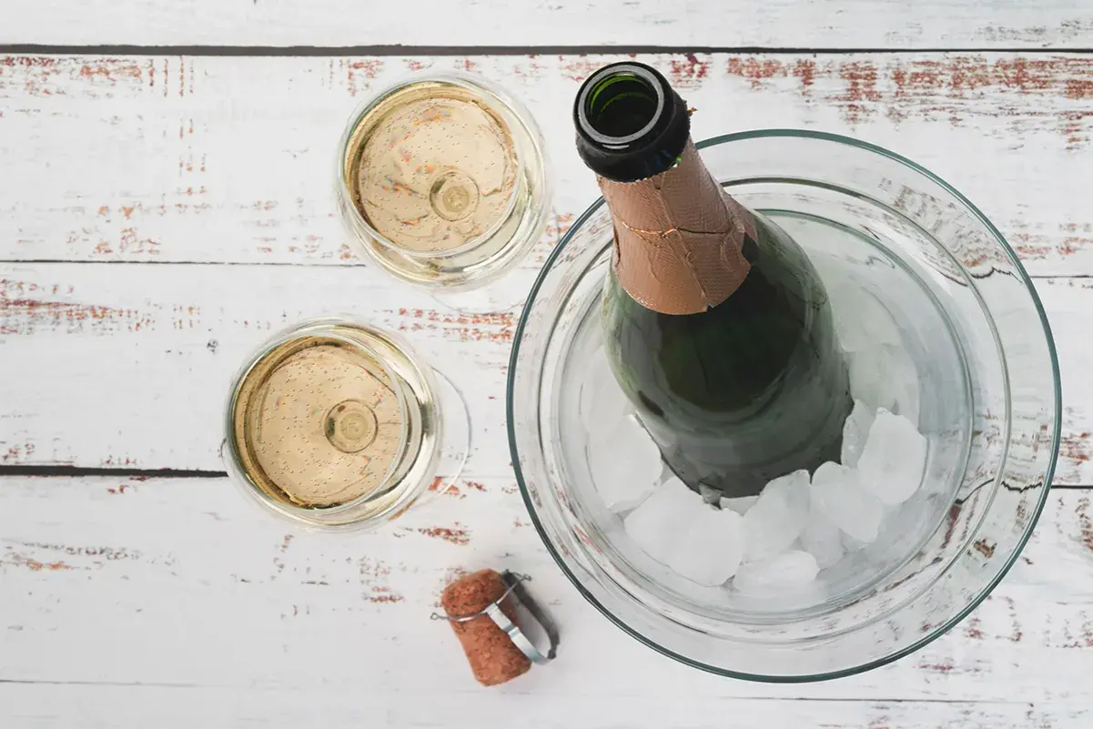 Due bicchieri di Prosecco e una bottiglia in un secchiello di ghiaccio. La temperatura ideale per il Prosecco è tra 6-8 gradi.