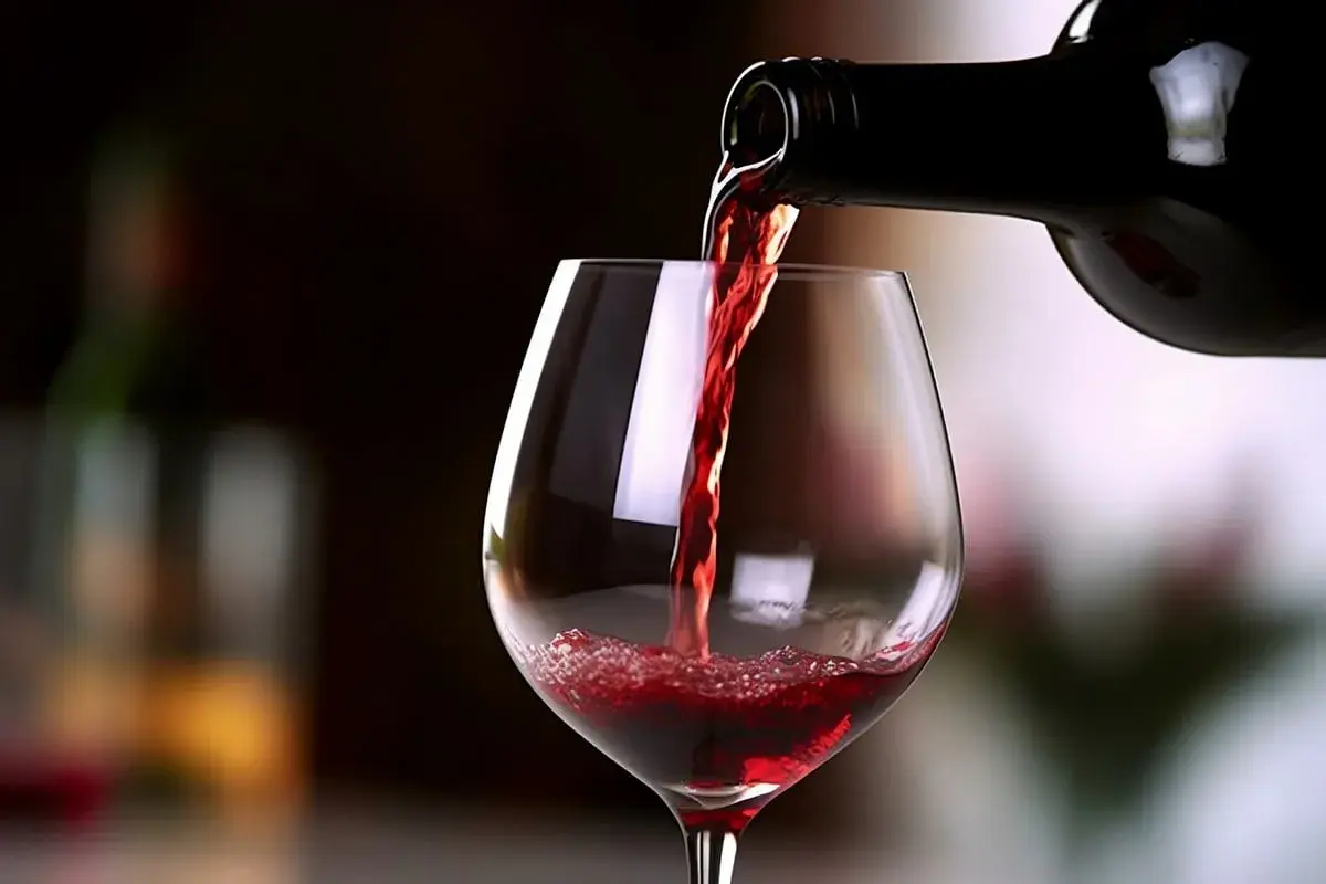 Versando un bicchiere di Carmignano vino rosso, con riflessi luminosi e una bottiglia scura sullo sfondo.