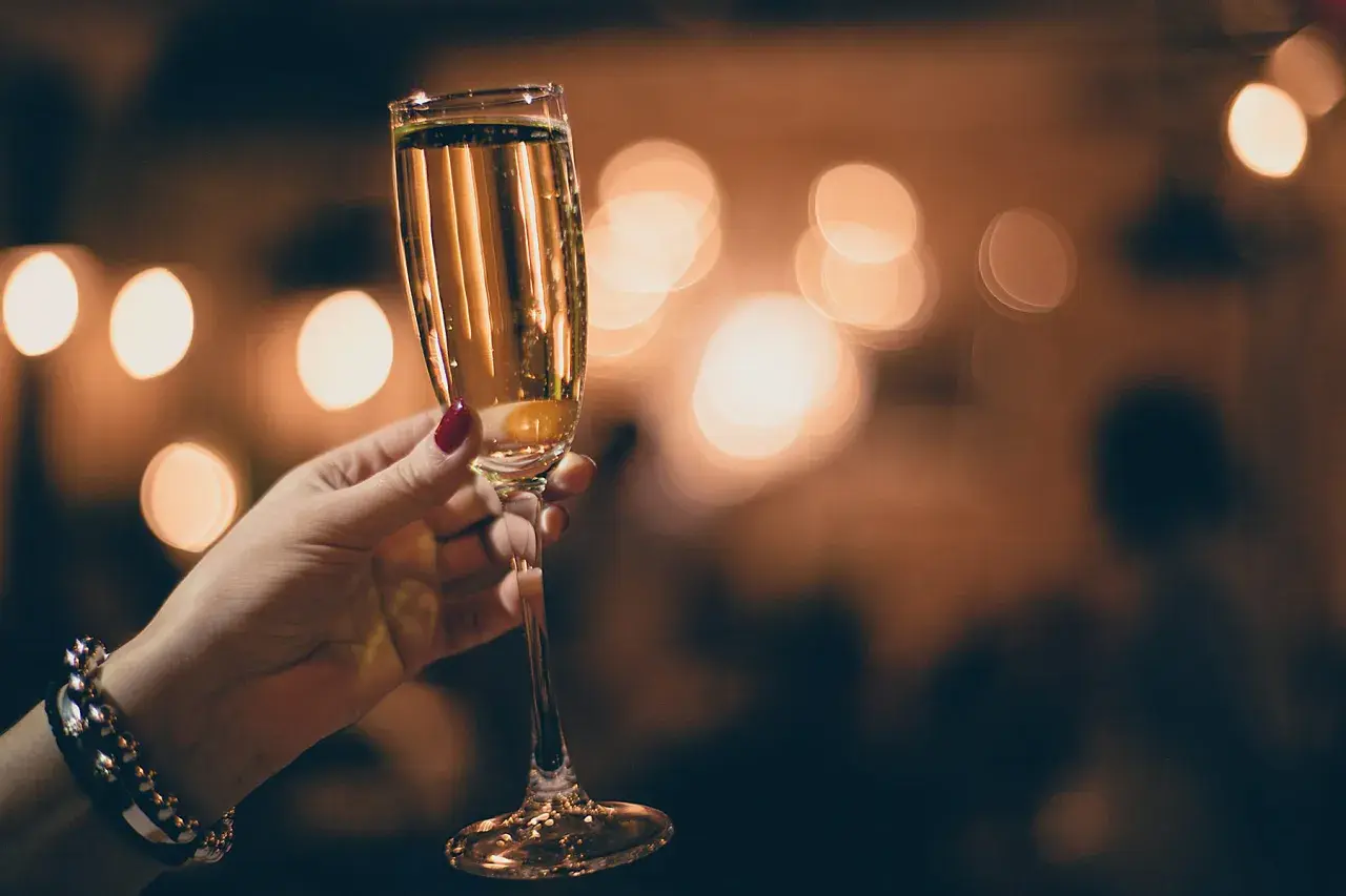 Mano con smalto rosso tiene un calice di champagne extra dry, con luci sfocate sullo sfondo.