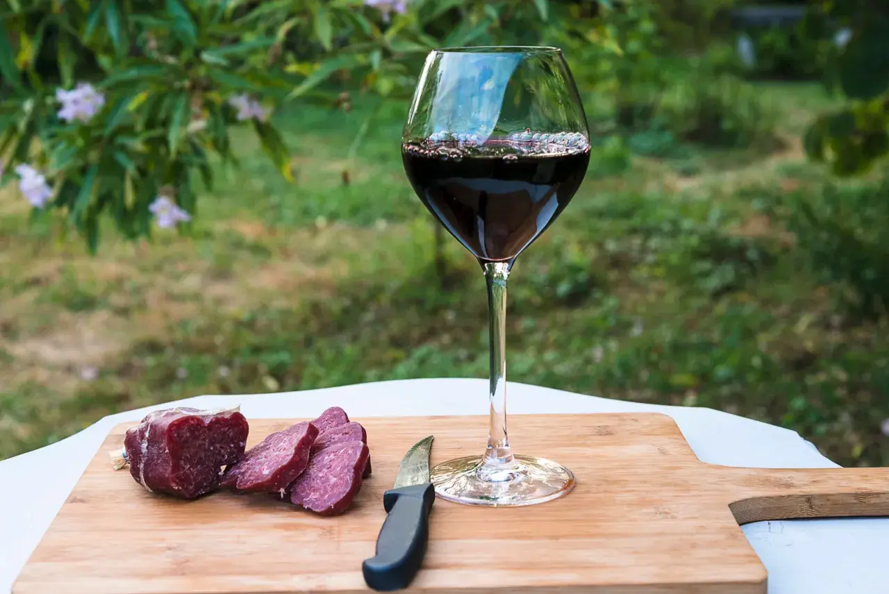 Un bicchiere di vino rosso e salumi affettati su un tagliere di legno, perfetti per le associazioni vini e salumi naturali.