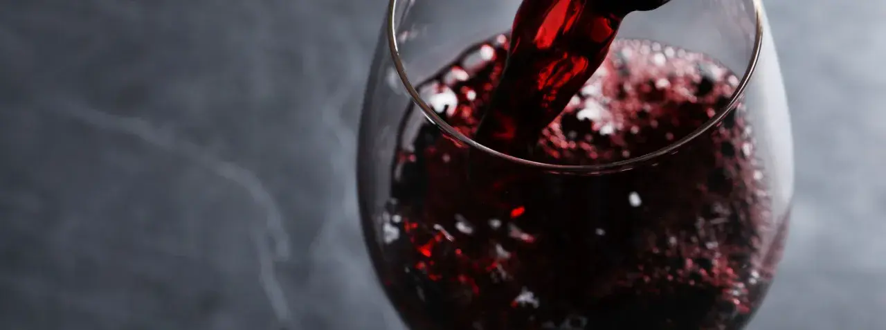 Versando vino rosso rubino in un calice, evocando i sapori autentici dei vini lucani.