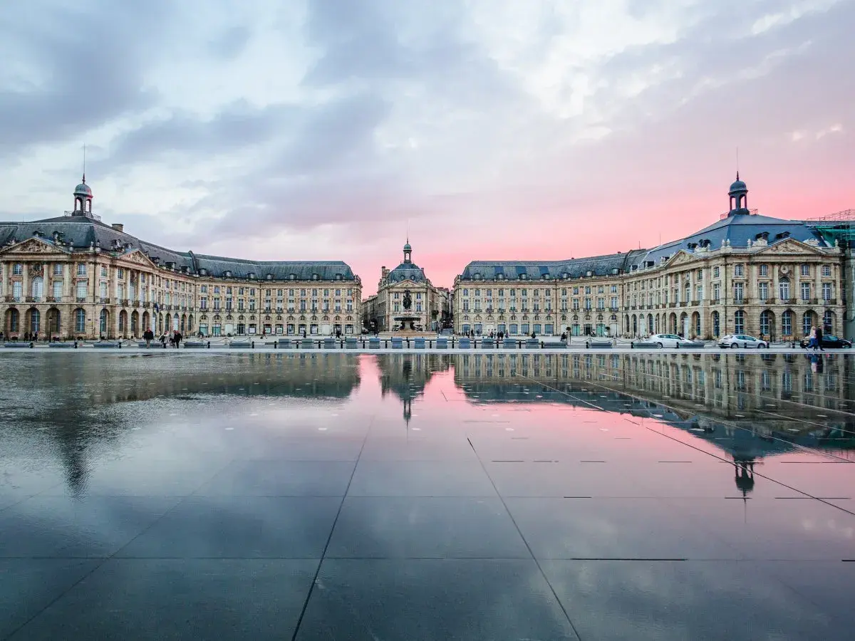 Piazza specchiata al tramonto, con edifici eleganti che ricordano il fascino del Medoc Bordeaux.