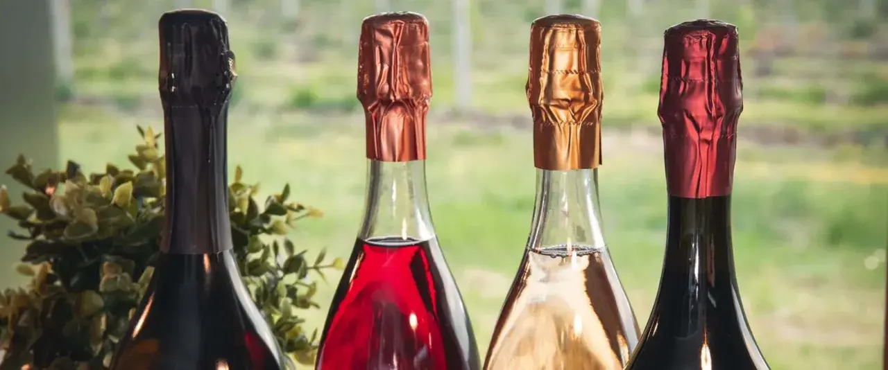 Quattro bottiglie di vini più pregiati, con tappi color rame, oro e rosso, pronte per essere degustate.