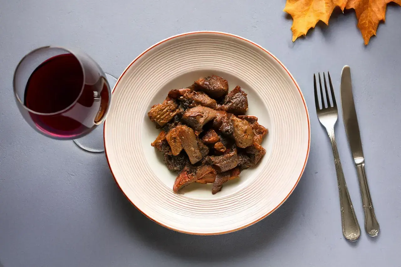 Piatto di cinghiale in umido con un bicchiere di vino rosso, perfetto vino da abbinare al cinghiale.
