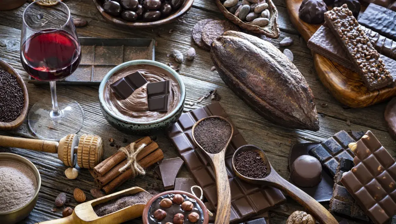 Un bicchiere di vino rosso accompagna una ricca selezione di cioccolato, dai chicchi di cacao alle tavolette, per un'esperienza golosa.