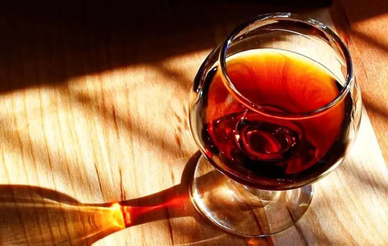Un bicchiere di **marsala vino** ambrato riposa su un tavolo di legno, illuminato da raggi di sole che creano ombre suggestive.