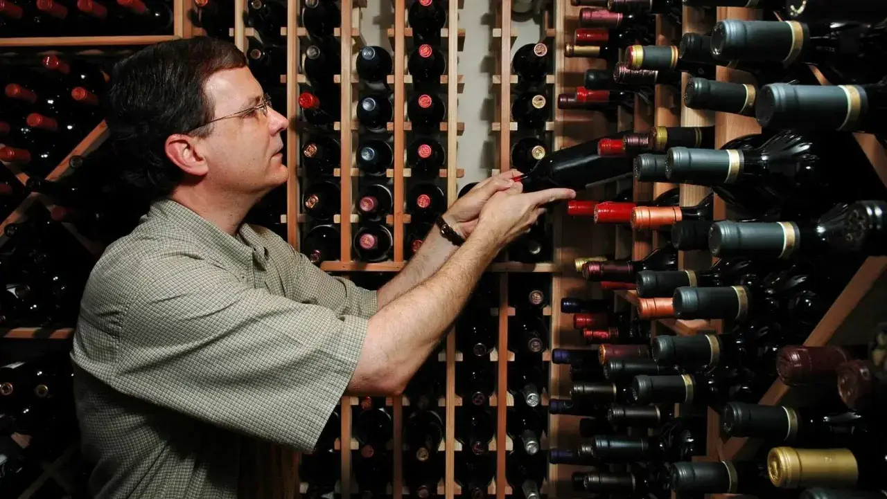 Uomo in cantina sceglie tra bottiglie di vino, tra cui uve cabernet.