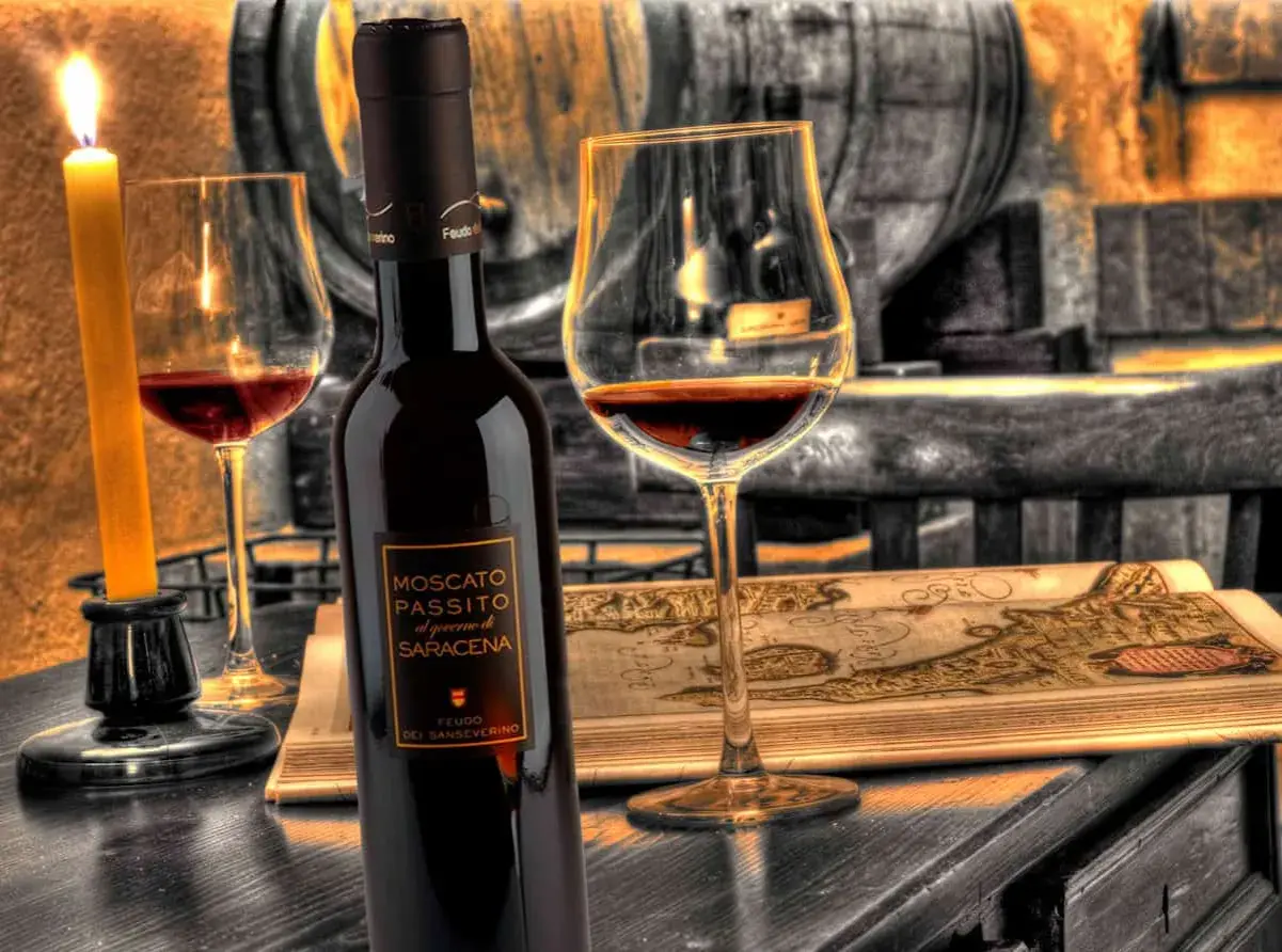 Una bottiglia e un calice di Moscato di Scanzo, illuminati da una candela, su un tavolo con una mappa antica.