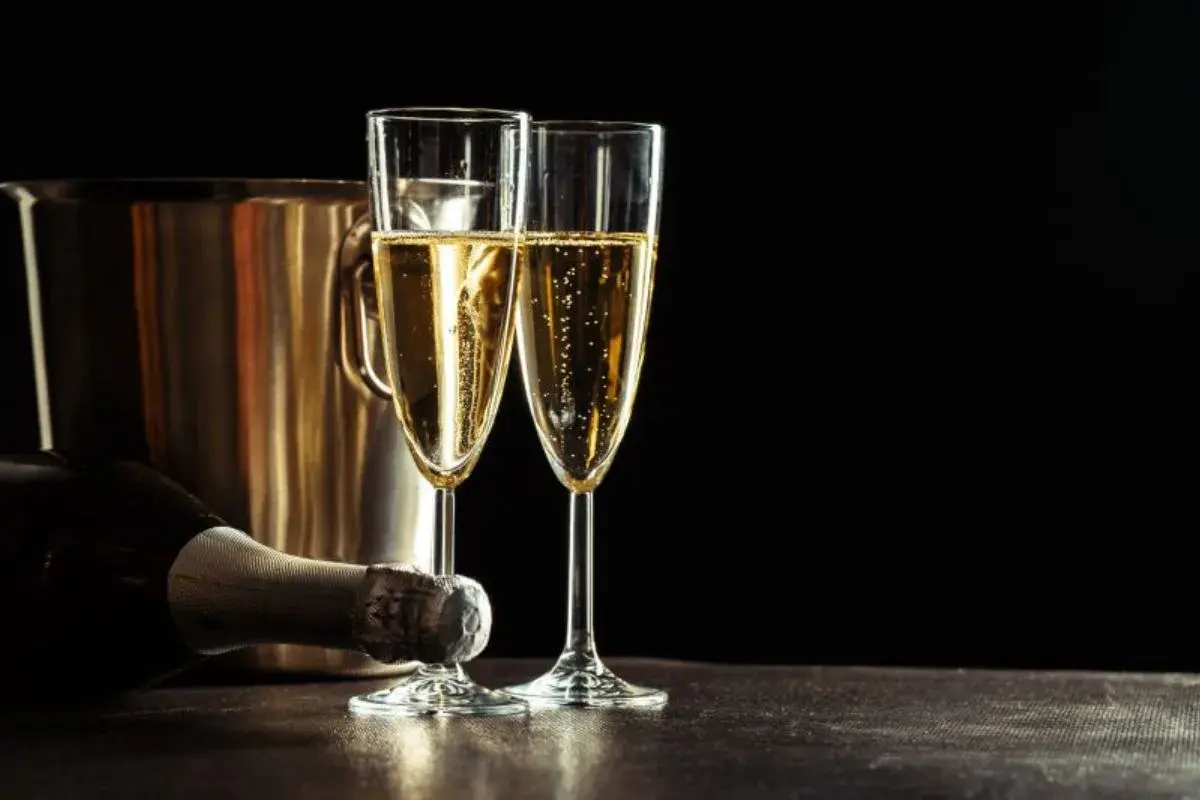 Due calici di champagne scintillante, una bottiglia e un secchiello per il ghiaccio. Un'uva per lo champagne, pronta per essere gustata.