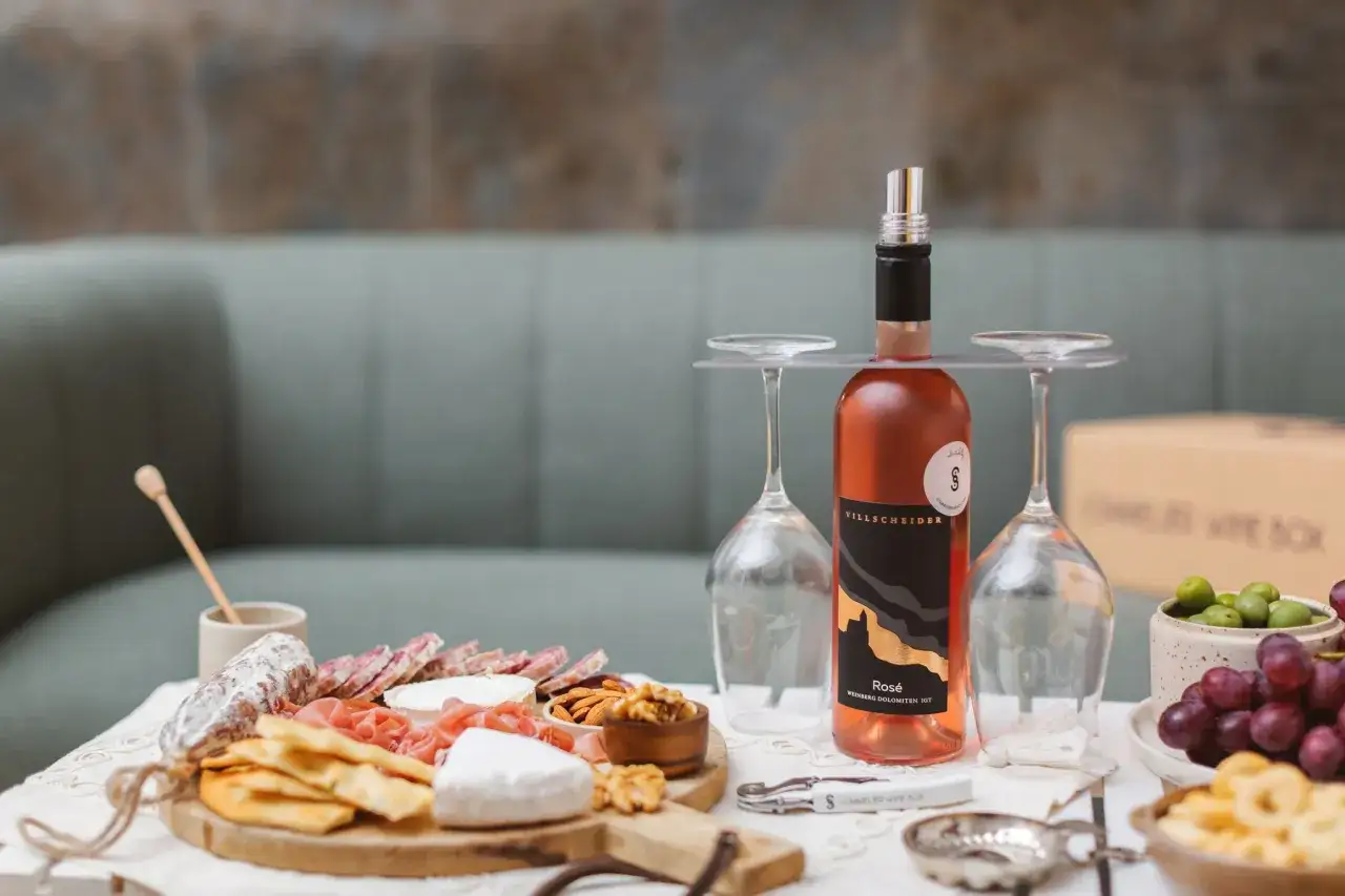 Un bicchiere di vino rosato, perfetto per i tuoi vini da aperitivo, accanto a un tagliere con salumi, formaggi e frutta.