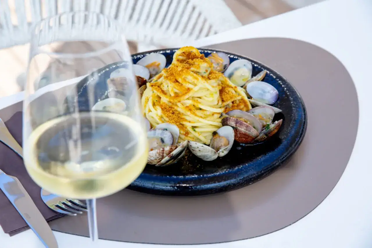 Spaghetti alle vongole con croccante pangrattato, un classico tra i vermentino abbinamenti. Un bicchiere di vino bianco accompagna il piatto.