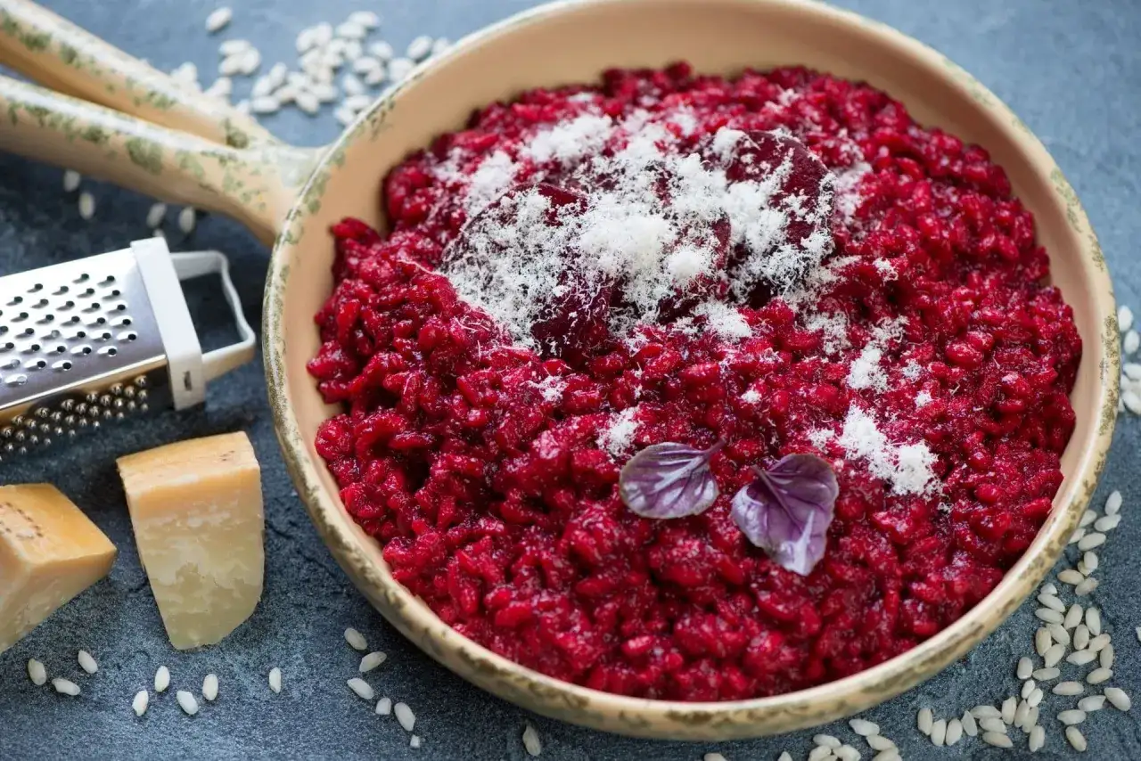 Risotto rosso vibrante, guarnito con parmigiano grattugiato e basilico. Perfetto con un bicchiere di vino rosso per risotto.
