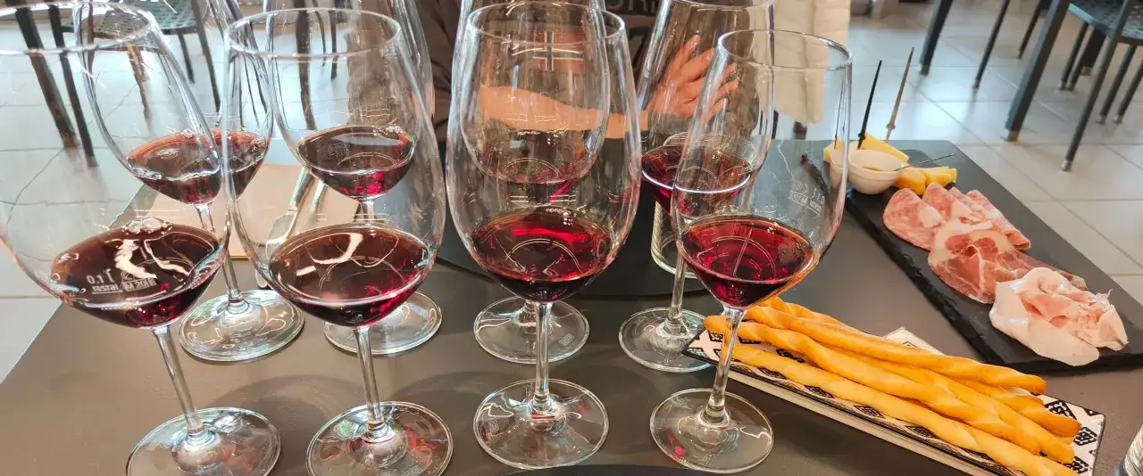 Calici di vino rosso, con riflessi rubino che evocano il colore del nebbiolo. Accanto, un tagliere con salumi e grissini.