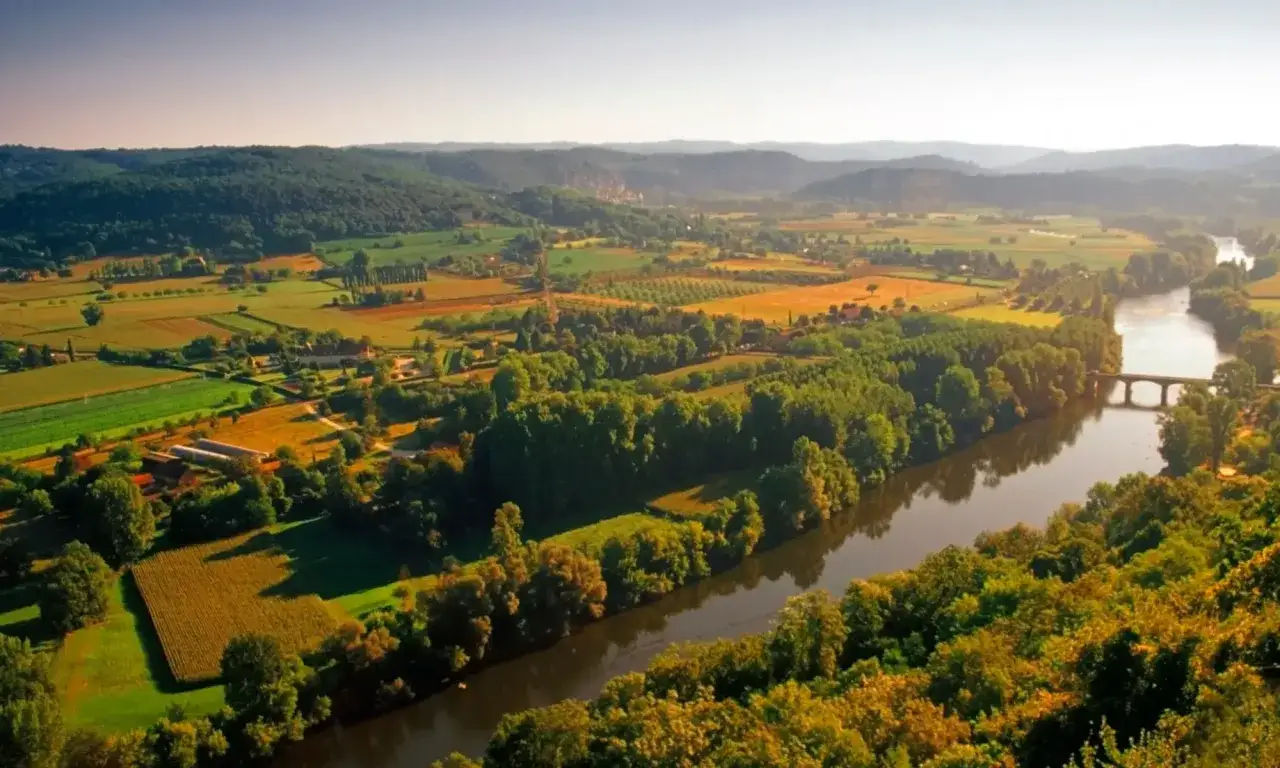 Vigneti rigogliosi e campi coltivati si estendono lungo un fiume serpeggiante, un paesaggio idilliaco che evoca il sapore del bergerac vino.