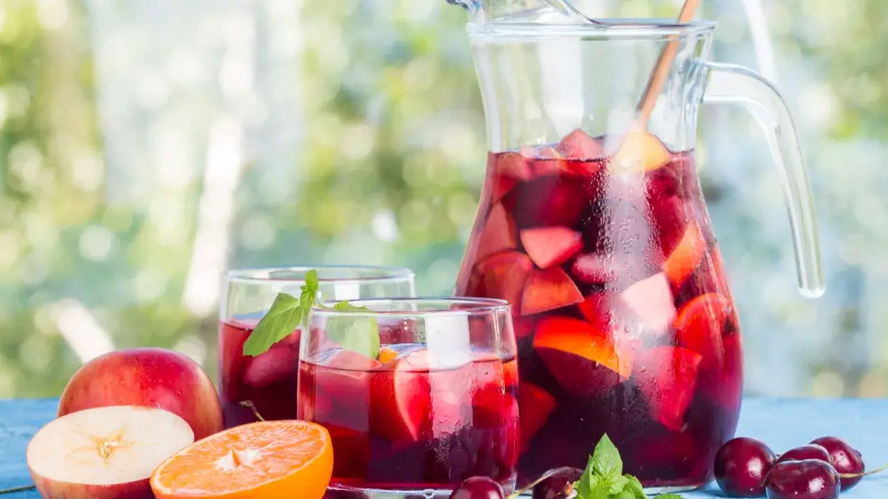 Rinfrescante sangria con prosecco, piena di frutta fresca come mele, arance e ciliegie, servita in un boccale e bicchieri.